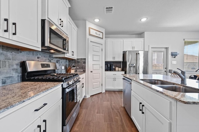170 Banff Dr, Kyle, TX 78640 - kitchen with appliances with stainless steel finishes, white cabinets, dark wood-style flooring, decorative backsplash, and light stone countertops