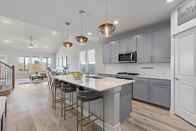3101 Maysilee St, Austin, TX 78728 - kitchen featuring stainless steel microwave, gray cabinets, open floor plan, light wood-style floors, and decorative backsplash