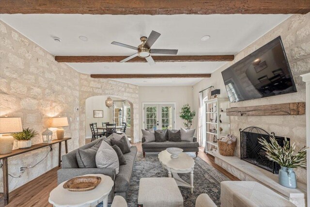 1660 W Mccarty Ln, San Marcos, TX 78666 - living room featuring wood finished floors, beamed ceiling, arched walkways, a fireplace with raised hearth, and ceiling fan