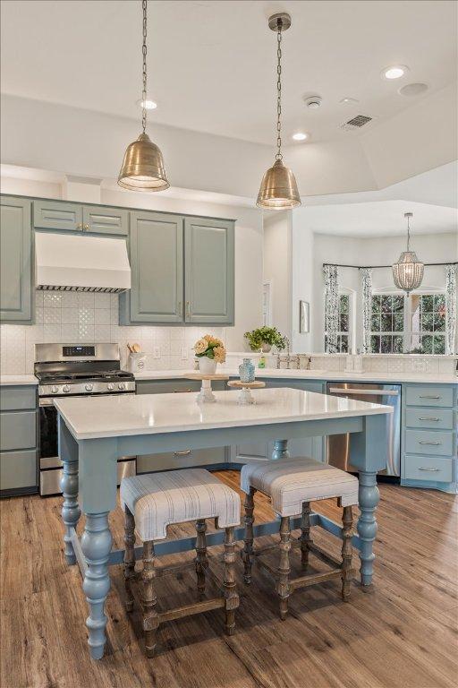 1660 W Mccarty Ln, San Marcos, TX 78666 - kitchen featuring custom exhaust hood, appliances with stainless steel finishes, light countertops, a breakfast bar area, and wood finished floors