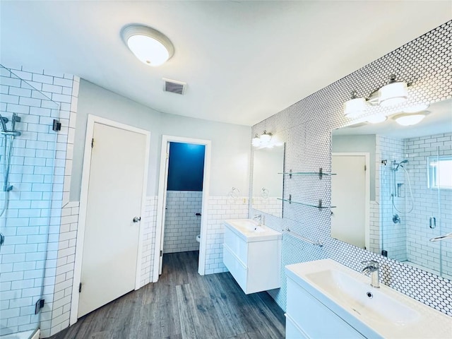 4202 Kilgore Ln, Austin, TX 78727 - full bathroom featuring tile walls, a stall shower, two vanities, wood finished floors, and a wainscoted wall