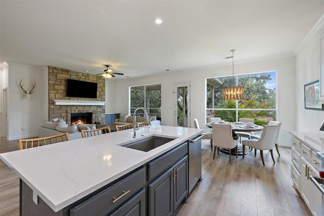 300 Errol Dr, Spicewood, TX 78669 - kitchen featuring a stone fireplace, crown molding, gray cabinetry, ceiling fan, and healthy amount of natural light