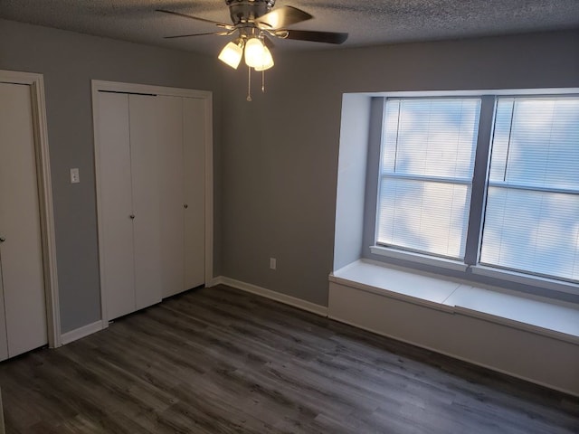 1221 W Hopkins St Unit 11, San Marcos, TX 78666 - unfurnished bedroom with dark wood-style floors, a textured ceiling, a ceiling fan, and multiple closets