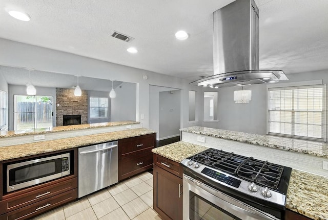 4614 Ganymede Dr, Austin, TX 78727 - kitchen with appliances with stainless steel finishes, island range hood, a fireplace, light stone countertops, and light tile patterned floors