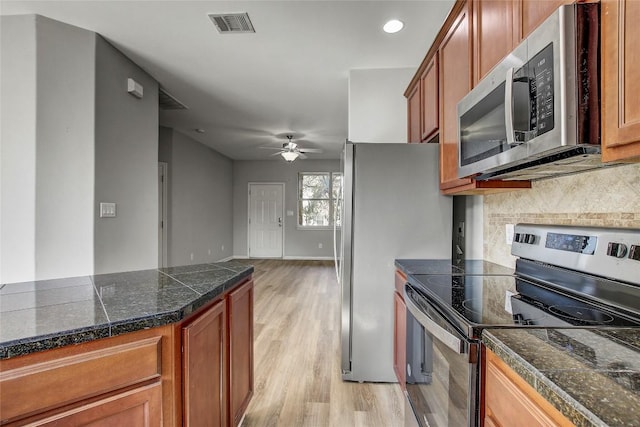 512 Eberhart Ln Unit 1207, Austin, TX 78745 - kitchen featuring stainless steel appliances, tile counters, light wood finished floors, a ceiling fan, and brown cabinetry