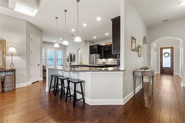 201 Glenfiddich Ln, Austin, TX 78738 - kitchen featuring arched walkways, freestanding refrigerator, dark stone countertops, dark wood-style floors, and a kitchen bar
