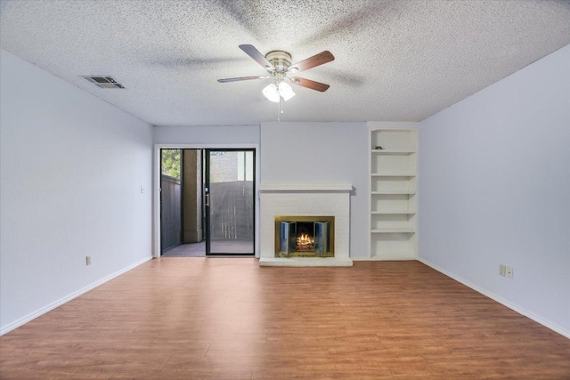 1202 Thorpe Ln Unit 407, San Marcos, TX 78666 - unfurnished living room featuring wood finished floors, built in shelves, a textured ceiling, ceiling fan, and a fireplace