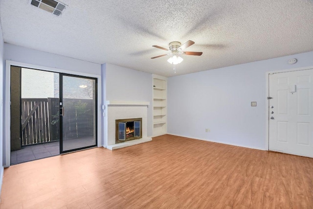 1202 Thorpe Ln Unit 407, San Marcos, TX 78666 - unfurnished living room with ceiling fan, wood finished floors, a textured ceiling, built in shelves, and a brick fireplace