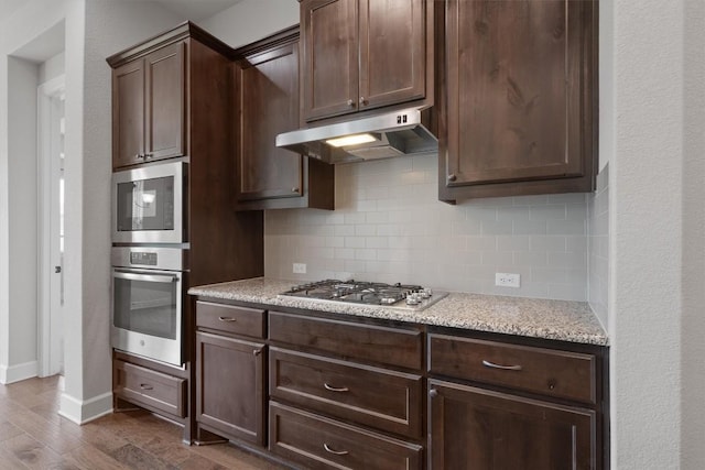416 Hereford Loop, Hutto, TX 78634 - kitchen featuring under cabinet range hood, stainless steel appliances, decorative backsplash, dark wood-type flooring, and dark brown cabinetry