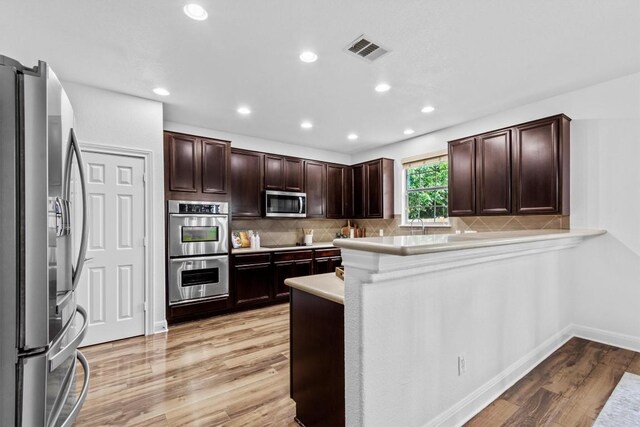 2003 Woodway Dr, Leander, TX 78641 - kitchen with appliances with stainless steel finishes, light wood finished floors, dark brown cabinetry, backsplash, and a peninsula