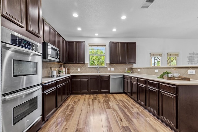 2003 Woodway Dr, Leander, TX 78641 - kitchen featuring appliances with stainless steel finishes, light wood-type flooring, light countertops, dark brown cabinetry, and recessed lighting