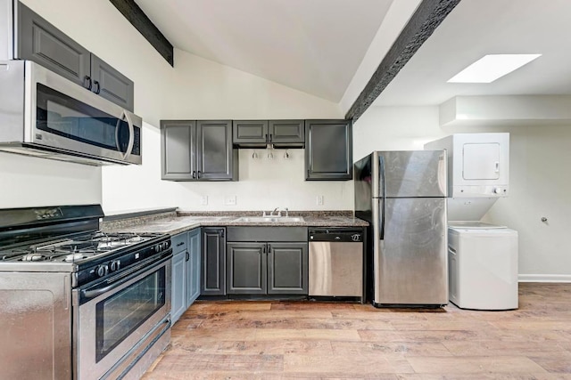 1010 W 23rd St Unit 2, Austin, TX 78705 - kitchen featuring stainless steel appliances, stacked washing machine and dryer, lofted ceiling, a skylight, and light wood-type flooring