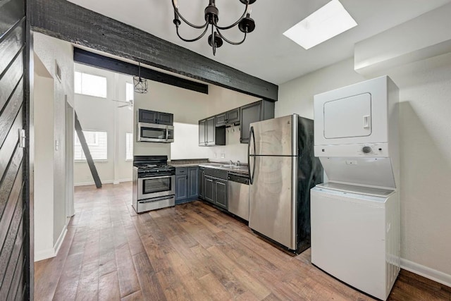 1010 W 23rd St Unit 2, Austin, TX 78705 - kitchen featuring stainless steel appliances, stacked washing machine and dryer, a skylight, gray cabinets, and wood finished floors