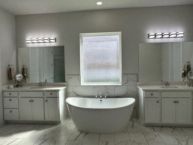 900 Elenora Dr, Leander, TX 78641 - full bath with marble finish floors, a freestanding tub, two vanities, tile walls, and recessed lighting