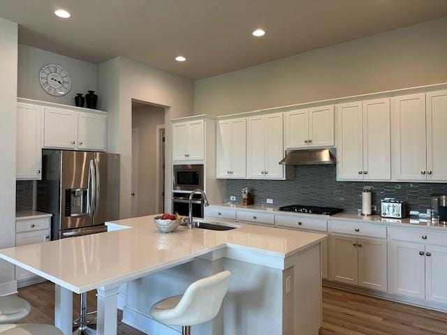 900 Elenora Dr, Leander, TX 78641 - kitchen featuring appliances with stainless steel finishes, under cabinet range hood, decorative backsplash, wood finished floors, and a kitchen bar