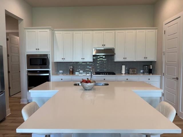 900 Elenora Dr, Leander, TX 78641 - kitchen featuring under cabinet range hood, stainless steel appliances, a breakfast bar, and wood finished floors