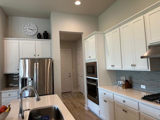 900 Elenora Dr, Leander, TX 78641 - kitchen featuring stainless steel appliances, light countertops, white cabinetry, backsplash, and wood finished floors