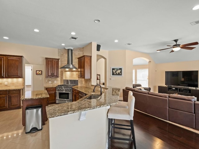 2520 Butler National Dr, Pflugerville, TX 78660 - kitchen with wall chimney range hood, high end stove, arched walkways, a ceiling fan, and light stone counters