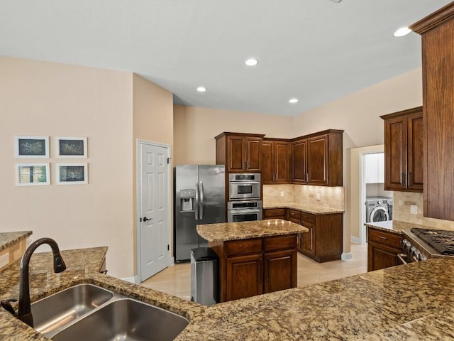 2520 Butler National Dr, Pflugerville, TX 78660 - kitchen featuring stainless steel appliances, washer / dryer, decorative backsplash, stone counters, and a kitchen island