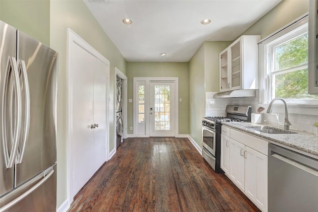 4412 Red River St, Austin, TX 78751 - kitchen with stainless steel appliances, stacked washing machine and dryer, light stone countertops, under cabinet range hood, and dark wood-style flooring