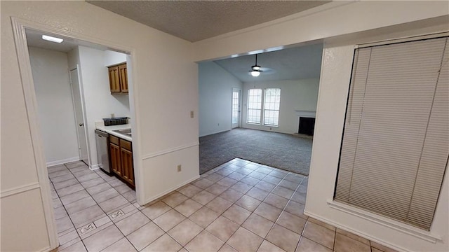 kitchen featuring stainless steel dishwasher, a ceiling fan, light colored carpet, light tile patterned floors, and a fireplace with raised hearth