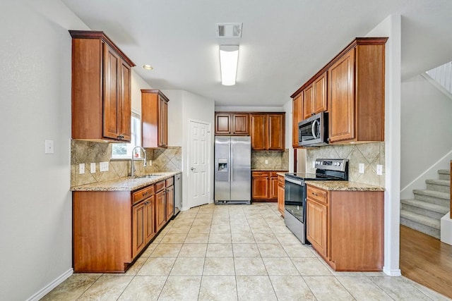 1921 Sand Creek Rd, Cedar Park, TX 78613 - kitchen featuring appliances with stainless steel finishes, decorative backsplash, light stone counters, and brown cabinetry