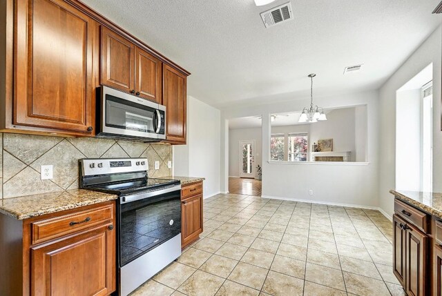 1921 Sand Creek Rd, Cedar Park, TX 78613 - kitchen with stainless steel appliances, a chandelier, decorative backsplash, light tile patterned flooring, and light stone counters
