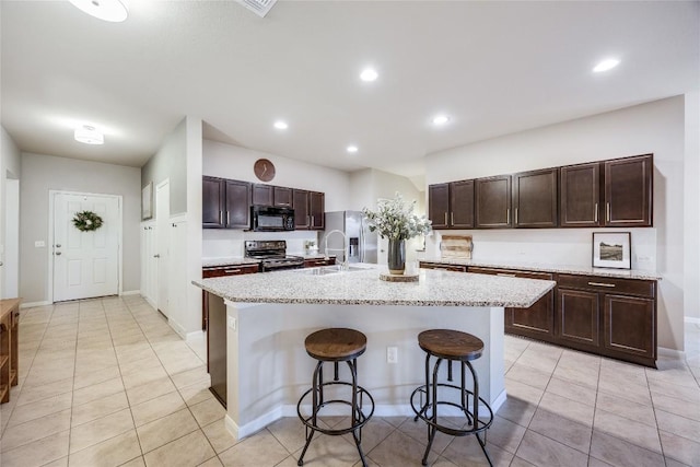 605 Liard River Rd, Hutto, TX 78634 - kitchen featuring black appliances, a breakfast bar area, light tile patterned flooring, dark brown cabinets, and a kitchen island with sink