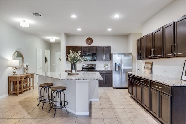 605 Liard River Rd, Hutto, TX 78634 - kitchen featuring black appliances, light tile patterned flooring, a breakfast bar, dark brown cabinetry, and recessed lighting