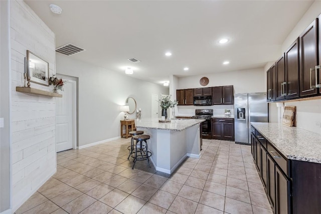 605 Liard River Rd, Hutto, TX 78634 - kitchen featuring black appliances, light tile patterned flooring, dark brown cabinetry, a kitchen breakfast bar, and a kitchen island