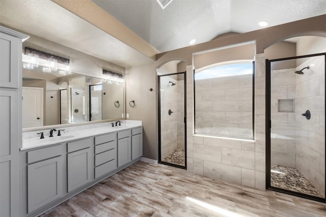 8305 Split Trail Cv, Temple, TX 76502 - bathroom with a shower stall, double vanity, wood finished floors, lofted ceiling, and a textured ceiling