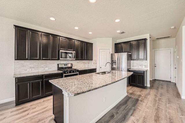 16912 Alturas Ave, Pflugerville, TX 78660 - kitchen with stainless steel appliances, backsplash, light stone counters, a center island with sink, and light wood-style flooring
