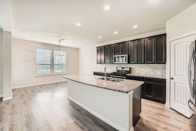 16912 Alturas Ave, Pflugerville, TX 78660 - kitchen featuring stainless steel appliances, tasteful backsplash, light stone countertops, light wood finished floors, and an island with sink