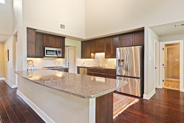 4104 Honeycomb Rock Cir, Austin, TX 78731 - kitchen with appliances with stainless steel finishes, dark wood finished floors, a towering ceiling, light stone countertops, and dark brown cabinetry