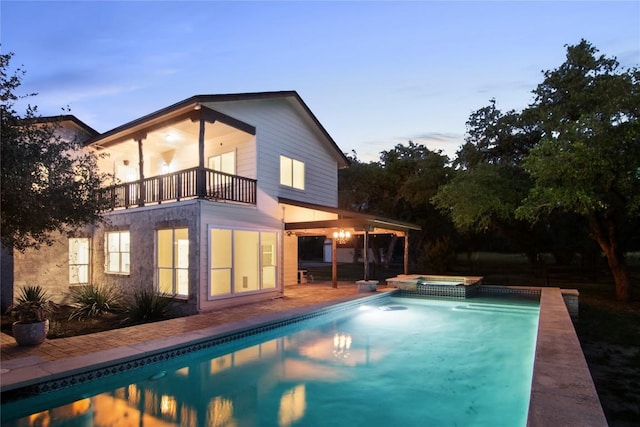 790 Enchanted Oaks Dr, Driftwood, TX 78619 - back of property at dusk featuring a balcony, a pool with connected hot tub, and a patio area