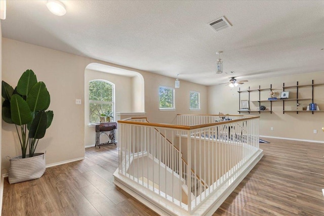 2818 Shadowpoint Cv, Round Rock, TX 78665 - hallway featuring an upstairs landing, wood finished floors, a textured ceiling, and arched walkways