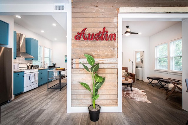 3405 Cedar St, Austin, TX 78705 - kitchen featuring blue cabinets, wall chimney range hood, white appliances, dark wood-style flooring, and tasteful backsplash