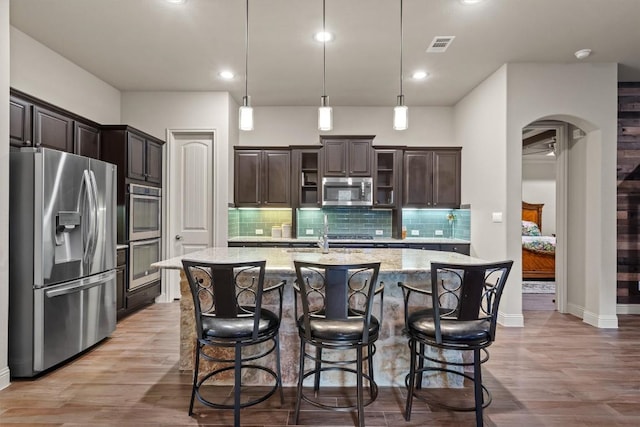 413 Fair Oaks Dr, Georgetown, TX 78628 - kitchen with stainless steel appliances, dark brown cabinets, decorative backsplash, a kitchen island with sink, and light wood-style flooring