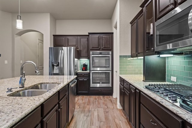 413 Fair Oaks Dr, Georgetown, TX 78628 - kitchen with appliances with stainless steel finishes, light wood-style floors, arched walkways, dark brown cabinetry, and decorative backsplash