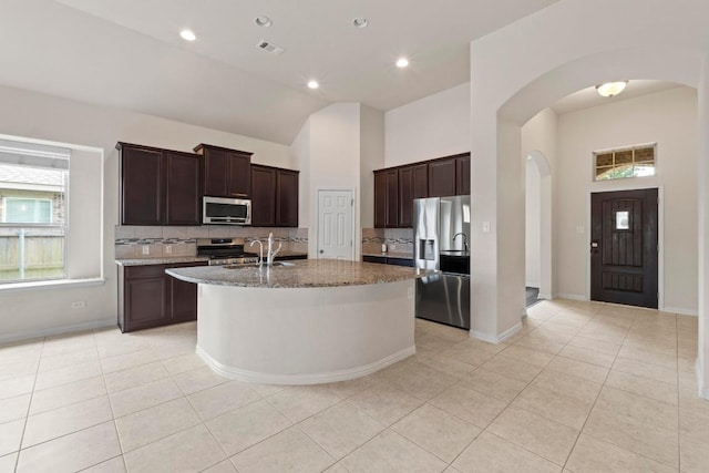 6042 Roma St, Round Rock, TX 78665 - kitchen featuring stainless steel appliances, arched walkways, backsplash, light tile patterned floors, and light stone counters