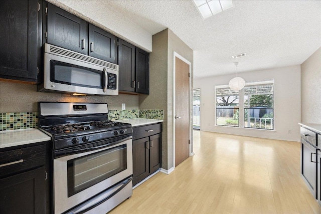 4910 Wing Rd, Austin, TX 78749 - kitchen with stainless steel appliances, light wood-style floors, backsplash, dark cabinets, and light countertops