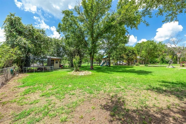 1004 Mitchell St, Gonzales, TX 78629 - view of yard featuring a trampoline, a playground, a storage unit, and view of wooded area