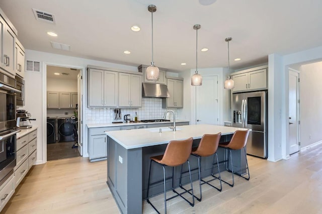 1209 Brasano Pl, Leander, TX 78641 - kitchen with appliances with stainless steel finishes, washing machine and dryer, under cabinet range hood, light wood finished floors, and recessed lighting