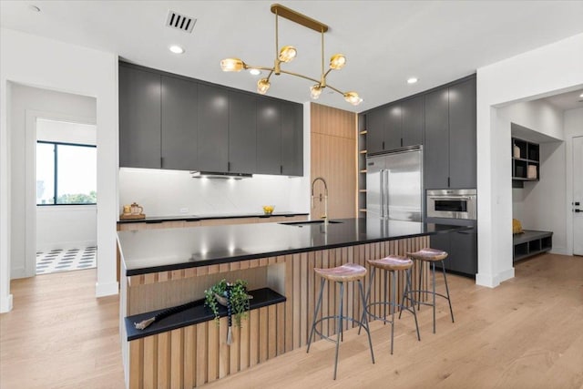 1000 Southlake Ranch Rd, Georgetown, TX 78628 - kitchen featuring stainless steel appliances, dark cabinets, light wood-style flooring, decorative backsplash, and a kitchen bar