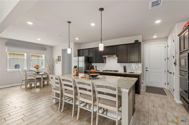 220 Bolivar Way Unit 101, San Marcos, TX 78666 - kitchen featuring appliances with stainless steel finishes, decorative backsplash, light wood finished floors, an island with sink, and a breakfast bar area