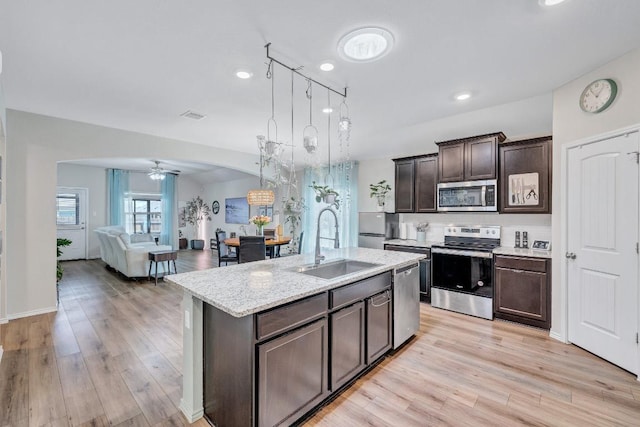 1904 T H Johnson Dr, Taylor, TX 76574 - kitchen featuring stainless steel appliances, arched walkways, dark brown cabinetry, light wood finished floors, and open floor plan