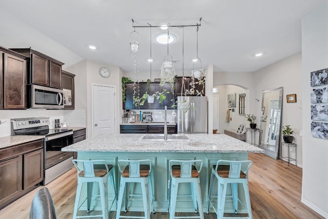 1904 T H Johnson Dr, Taylor, TX 76574 - kitchen with stainless steel appliances, dark brown cabinetry, a center island with sink, light stone counters, and arched walkways