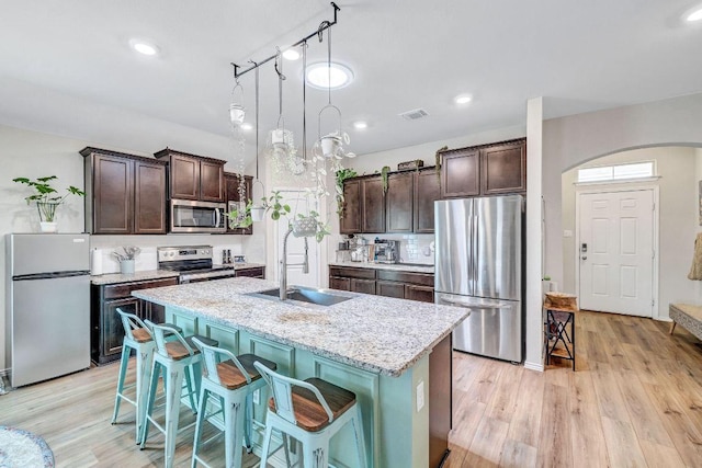 1904 T H Johnson Dr, Taylor, TX 76574 - kitchen with appliances with stainless steel finishes, dark brown cabinetry, arched walkways, light wood finished floors, and a center island with sink