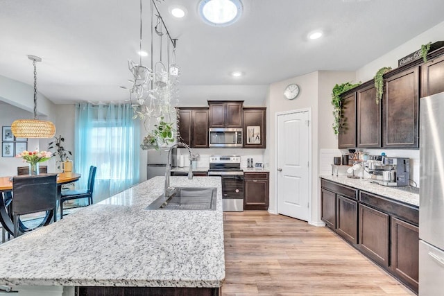 1904 T H Johnson Dr, Taylor, TX 76574 - kitchen with stainless steel appliances, dark brown cabinets, a kitchen island with sink, light wood-style flooring, and recessed lighting