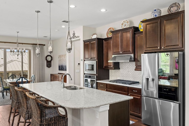 249 Hopping Peach St, San Marcos, TX 78666 - kitchen with appliances with stainless steel finishes, under cabinet range hood, dark wood-style flooring, an island with sink, and tasteful backsplash